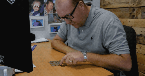 Man sat at his desk counting out the pennies he has set aside for his low cost website.